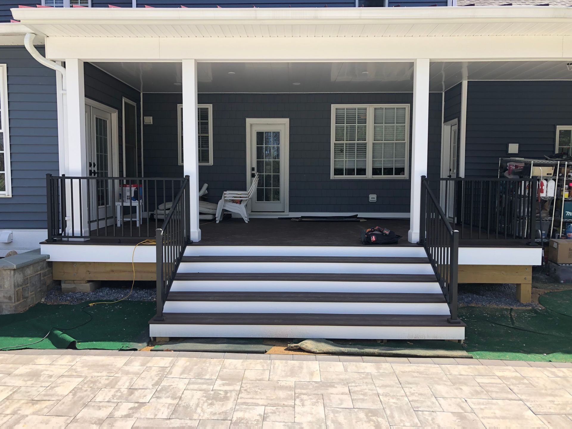 Covered porch with stairs and railing, dark gray siding. Brown and white steps, with black railings.