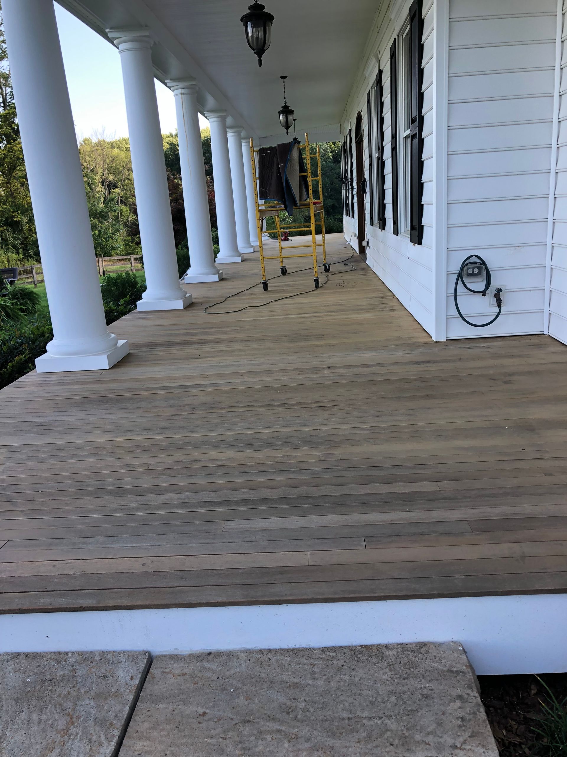 A weathered wooden porch with columns; a ladder and electrical meter are visible.