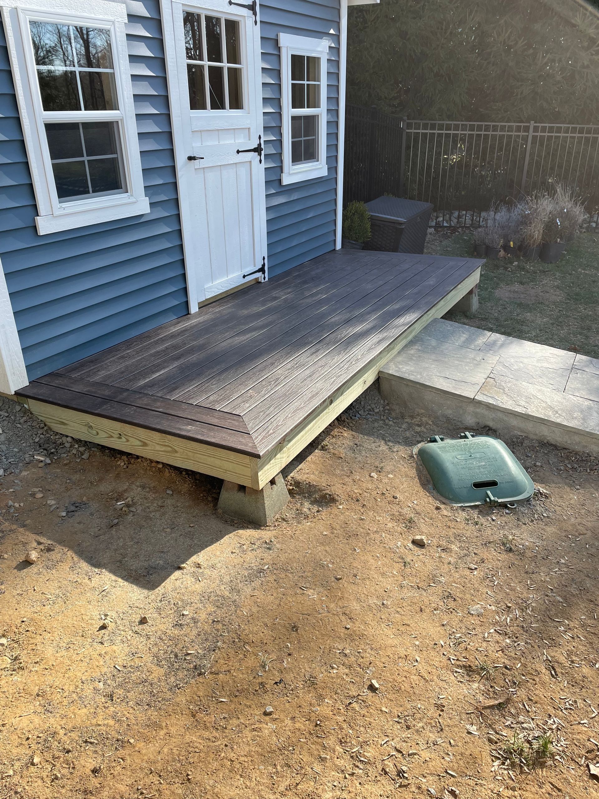 Blue building with white trim, a small deck with brown surface, and a concrete step.