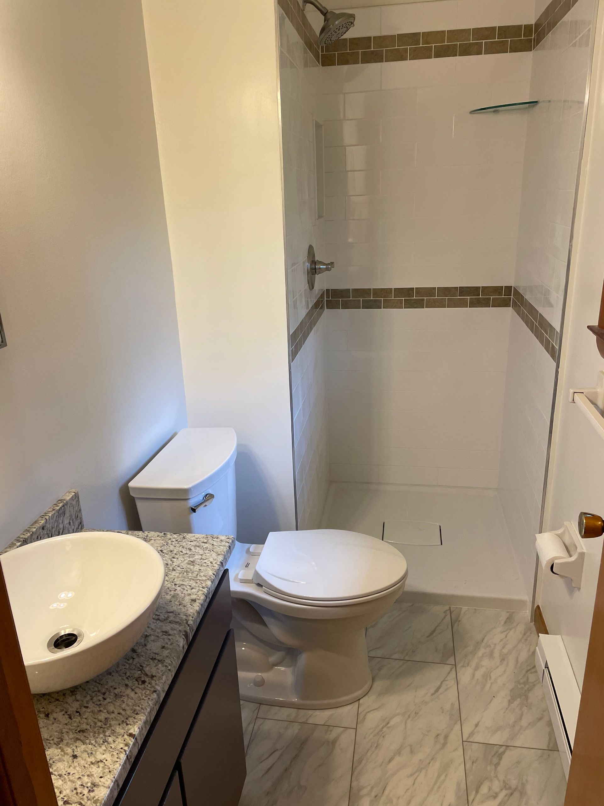 Bathroom with a white toilet, sink, and shower. The floor and shower trim have a marble design.