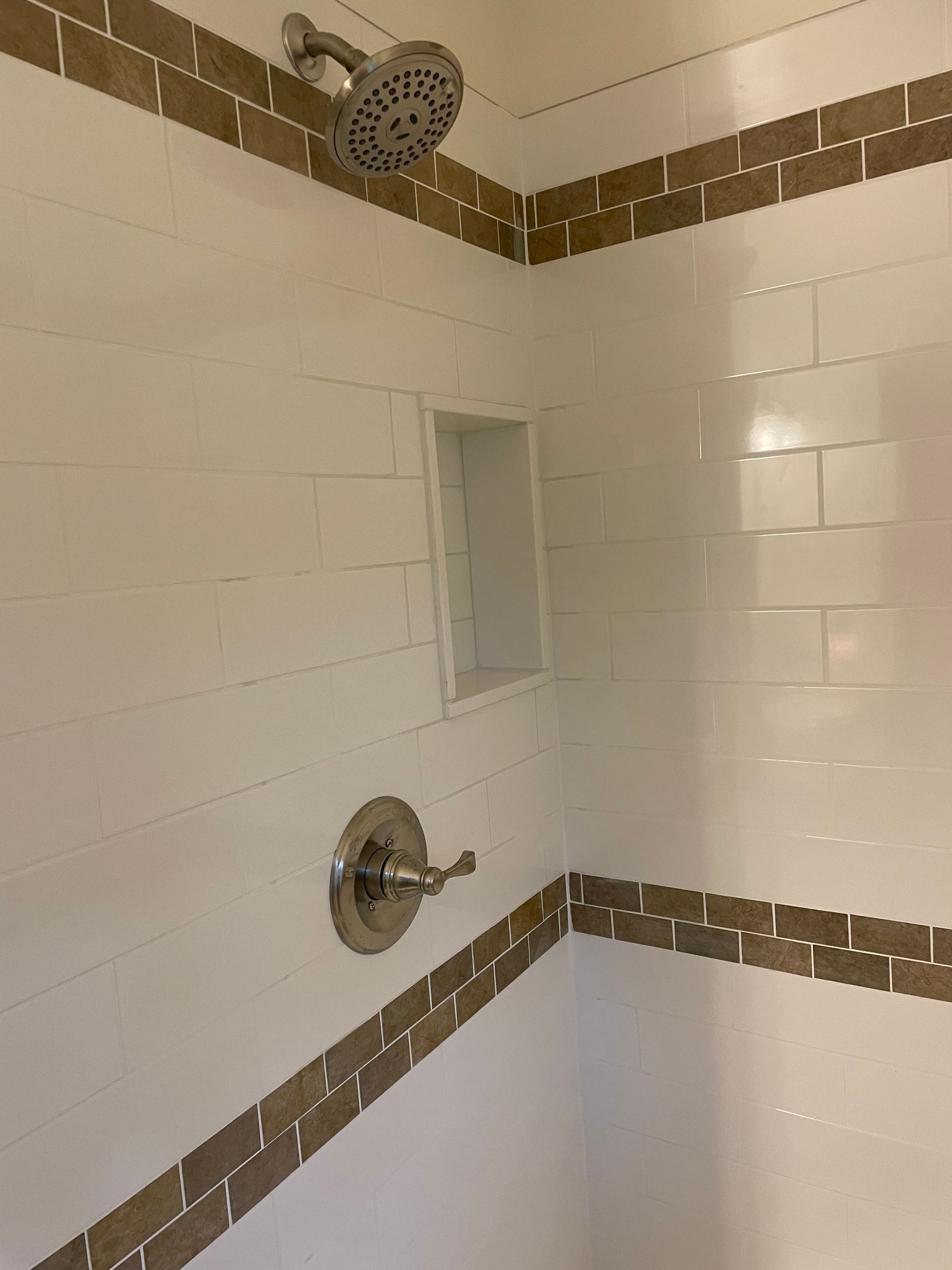 White-tiled shower with a recessed shelf, brown tile trim, and silver shower fixtures.