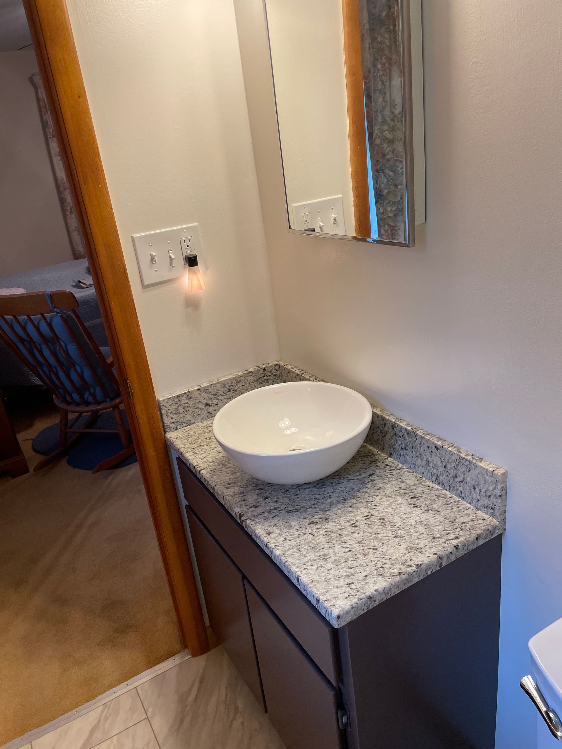 Bathroom vanity with a round white sink, gray countertop, and dark cabinets.