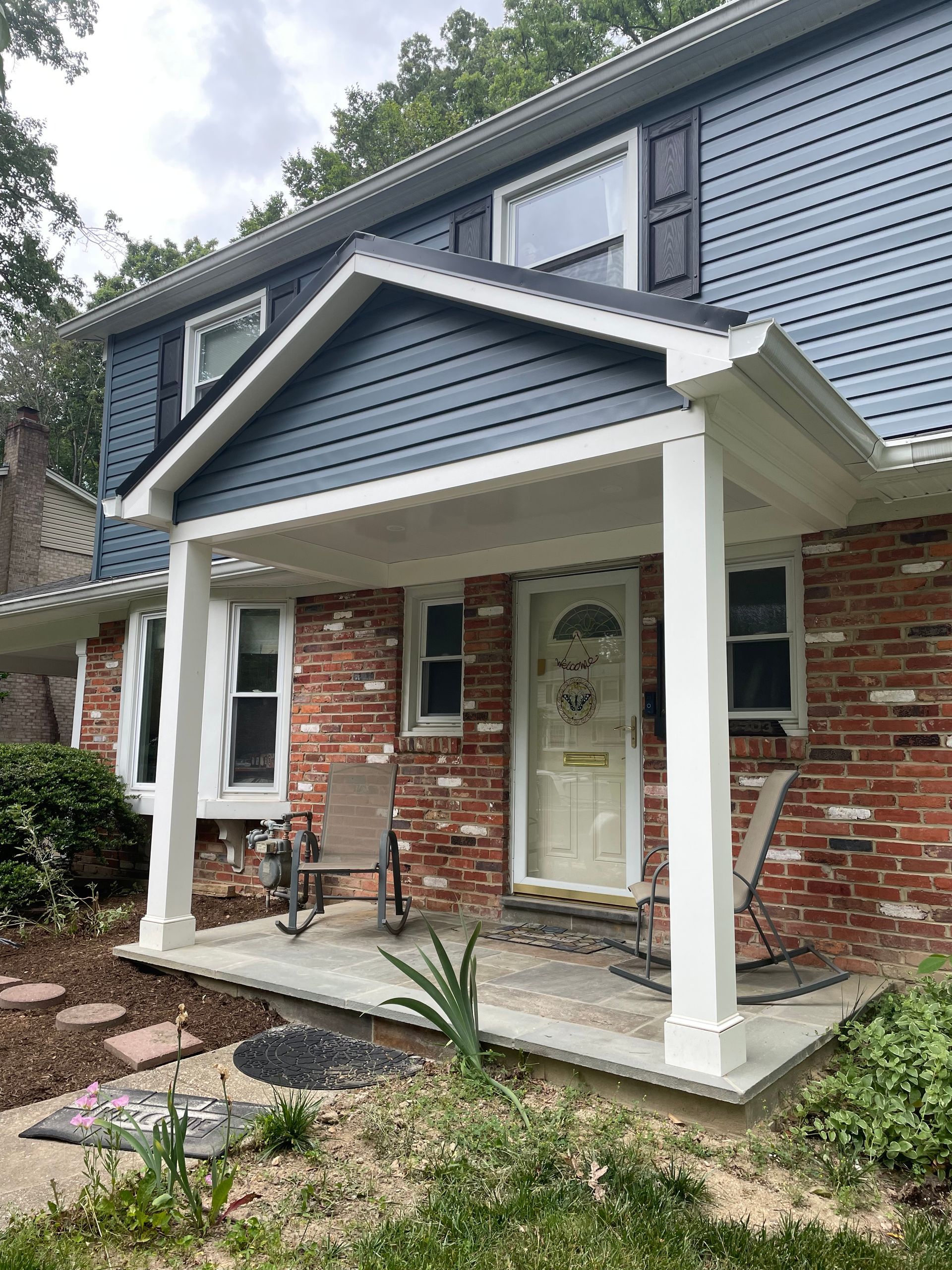 Brick house with blue siding, white porch posts, and a covered entrance.