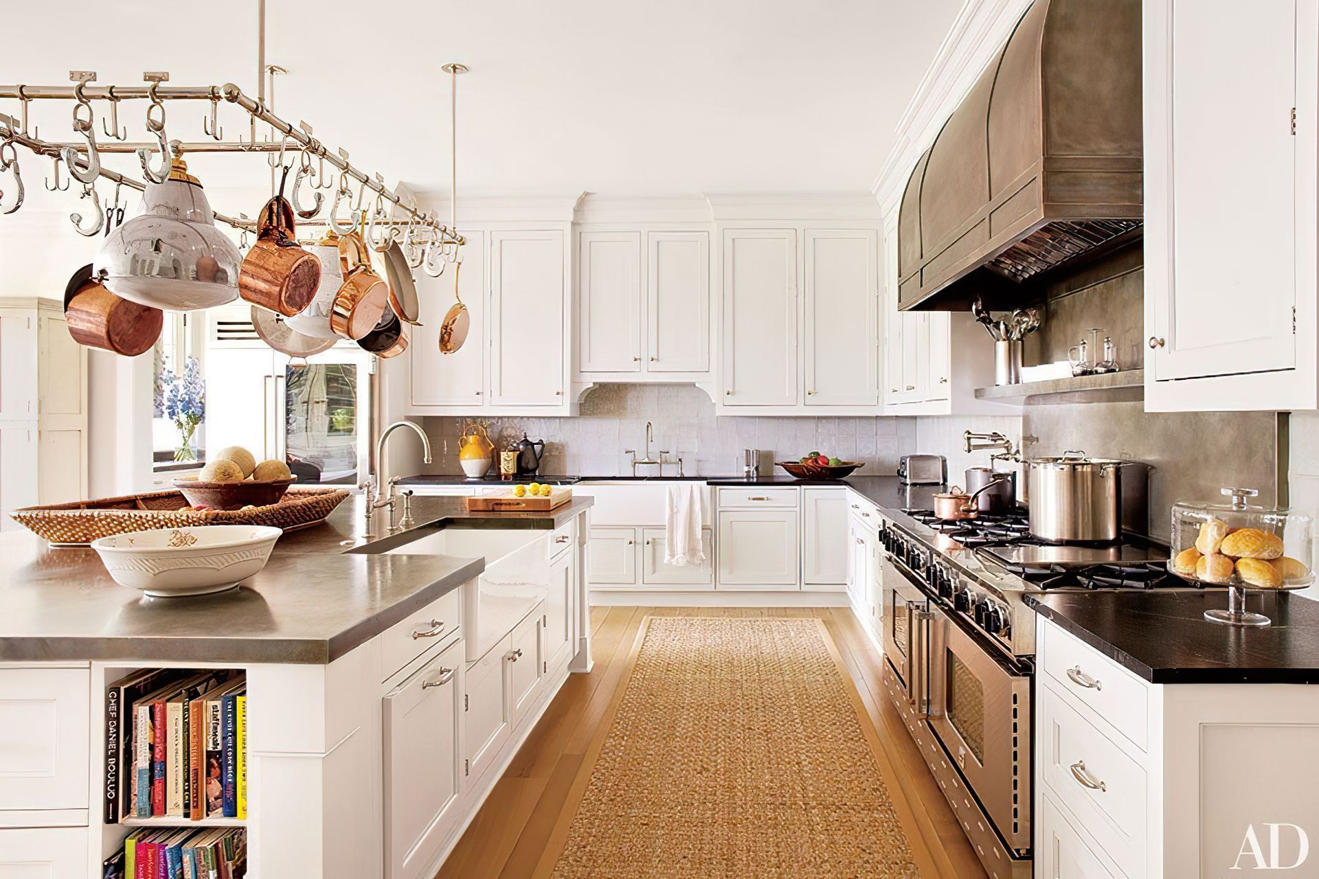 White kitchen with island, stainless steel range, and hanging pot rack.