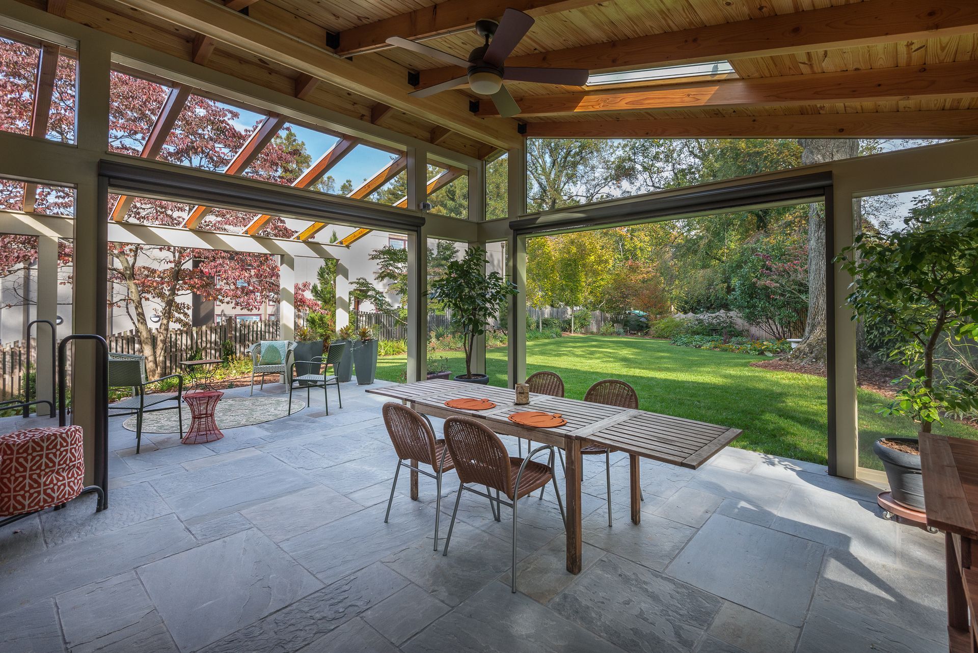 Outdoor dining area with a long table and chairs, overlooking a lush green yard and garden.