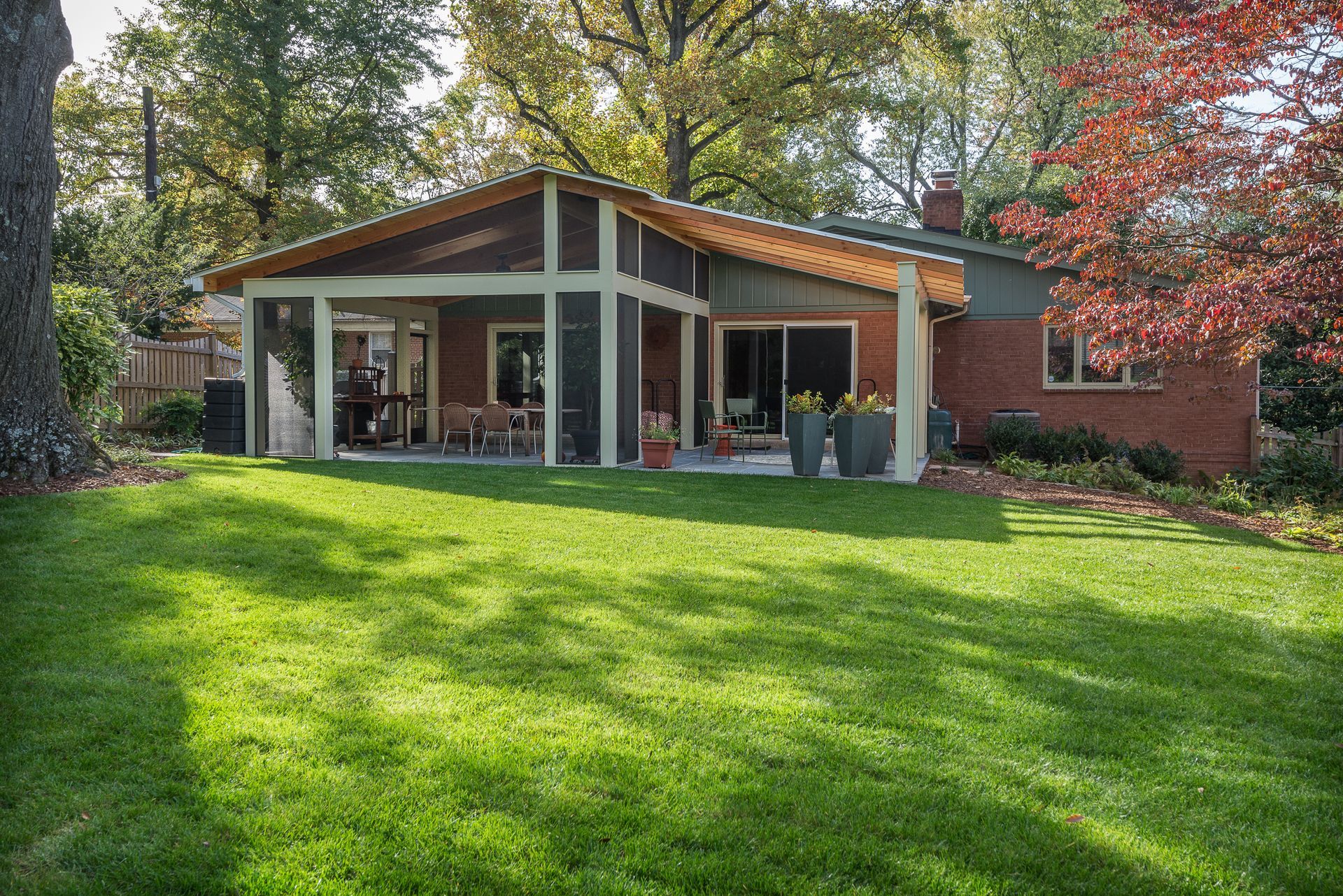 Backyard of a house with a screened-in porch, green lawn, trees, and red brick.
