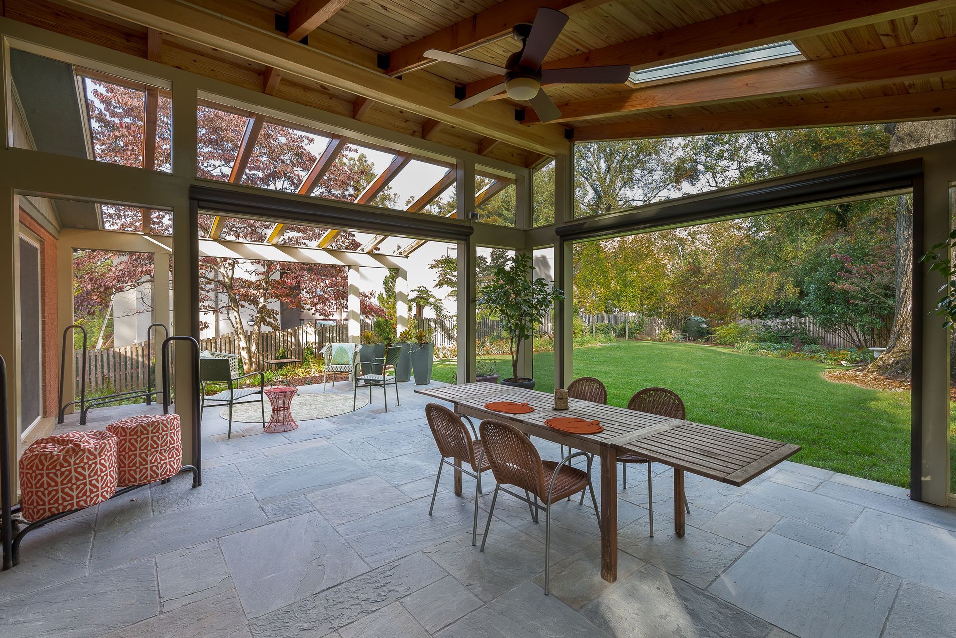 Outdoor patio with open glass walls, dining table, and view of a backyard.