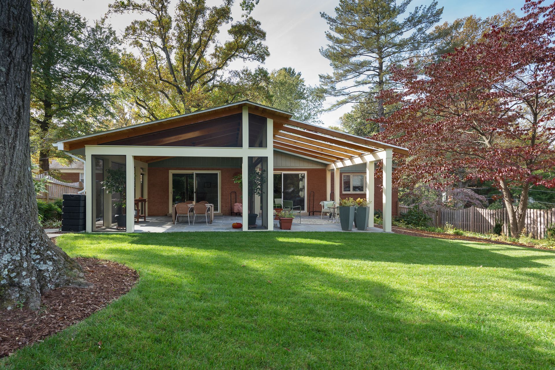 Backyard with house and screened-in porch; green lawn, trees, and patio furniture.