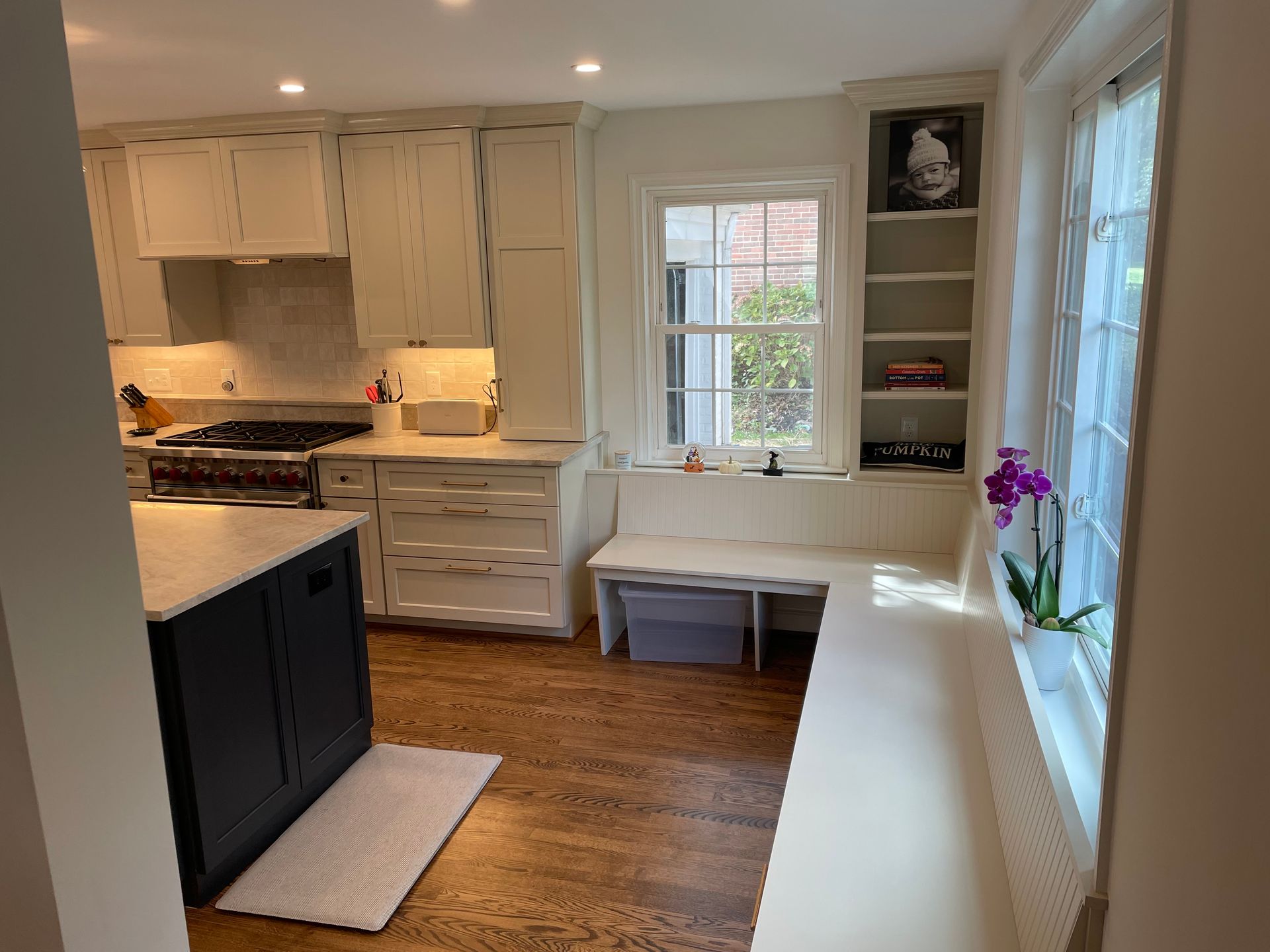 Kitchen with cream cabinets, dark island, window seat, and wood floors.