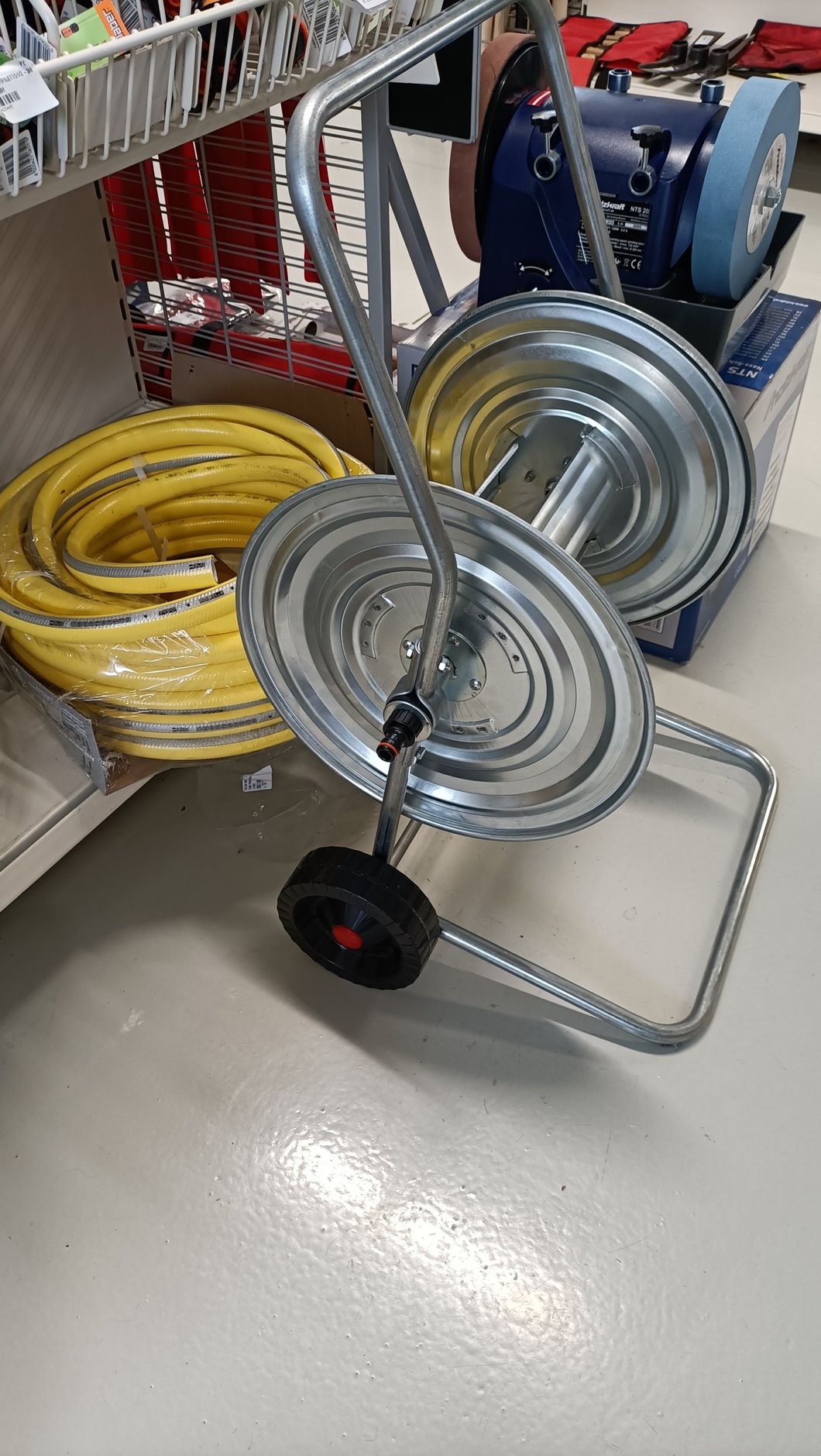 Carrello della spesa con tubo giallo arrotolato e avvolgitubo metallico impilati in una corsia del negozio.