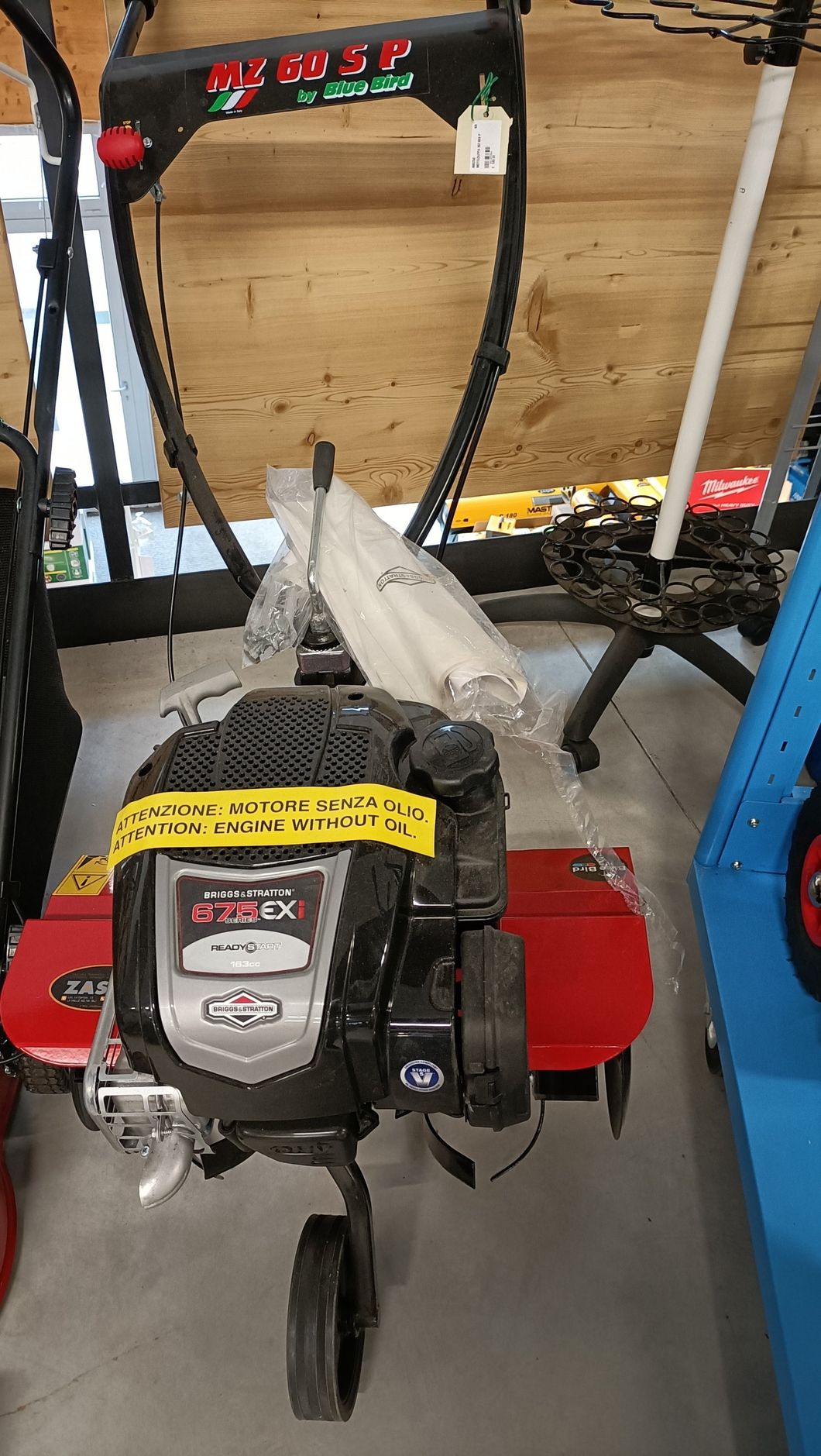 Piccola macchina rossa e nera con serbatoio e tubo del carburante, appoggiata su uno scaffale in un'officina o in un garage.