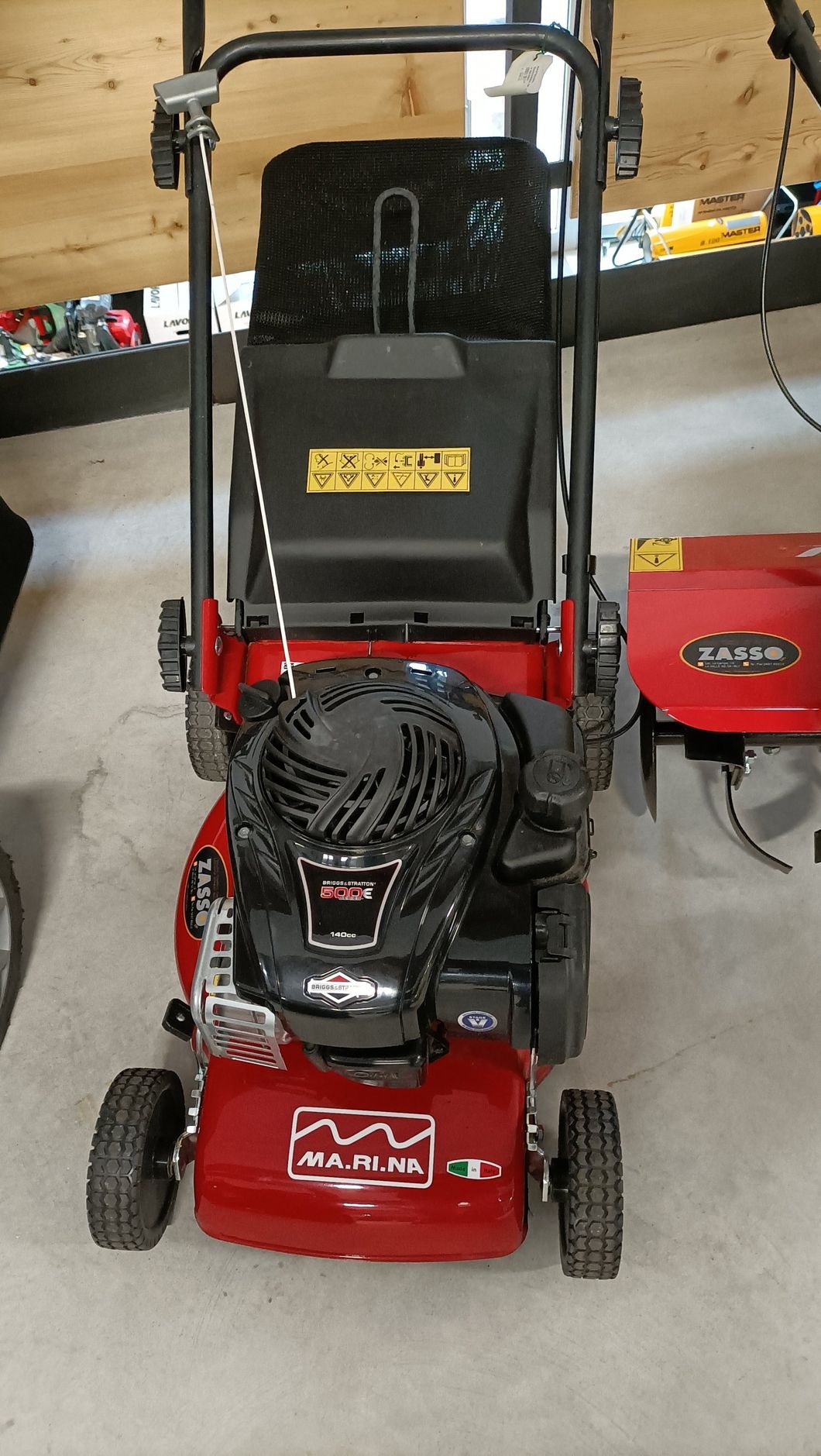 Tosaerba rosso e nero con sacco raccoglierba in un garage o in un'officina.