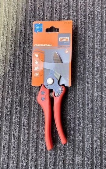 Forbici da potatura con manico rosso, in confezione arancione, su un tappeto grigio.
