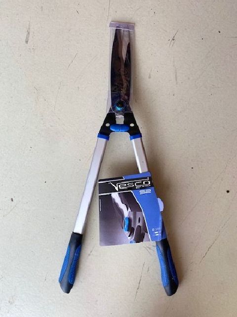 Forbici da potatura con manico blu appese a una parete, con l'etichetta del prodotto attaccata.