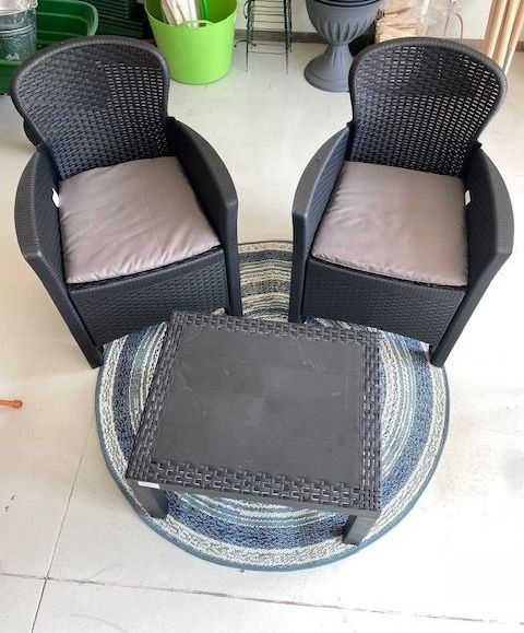 Due sedie in vimini nere con cuscini beige disposte attorno a un tavolino rotondo blu su un patio piastrellato.