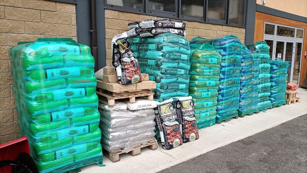 Pile di sacchi verdi di cibo per animali e pallet allineati contro la facciata di un edificio.