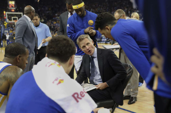 Golden State Warriors coach strategizing in the middle of a huddle of NBA basketball players
