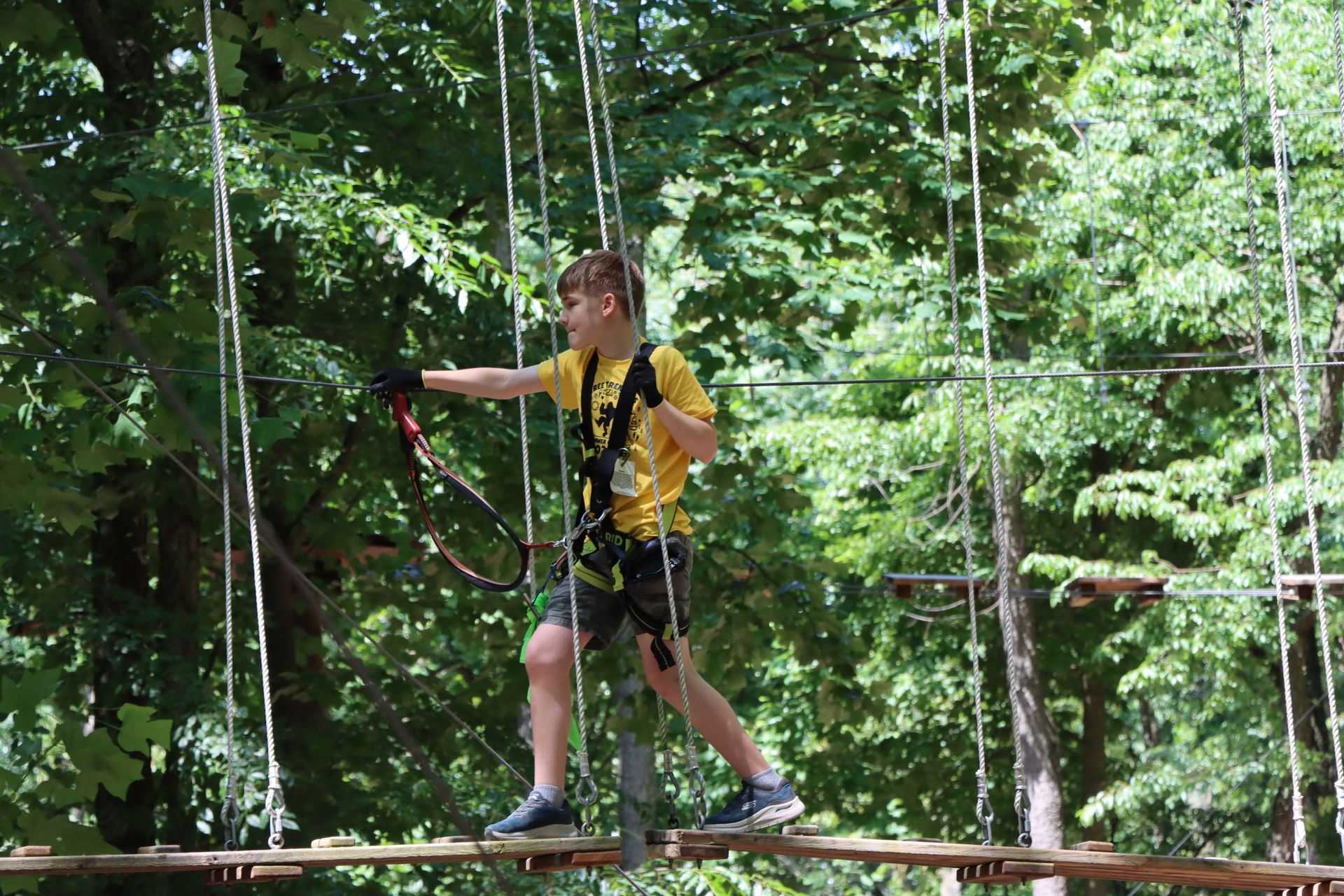 A young boy is walking across a ropes course in the woods.
