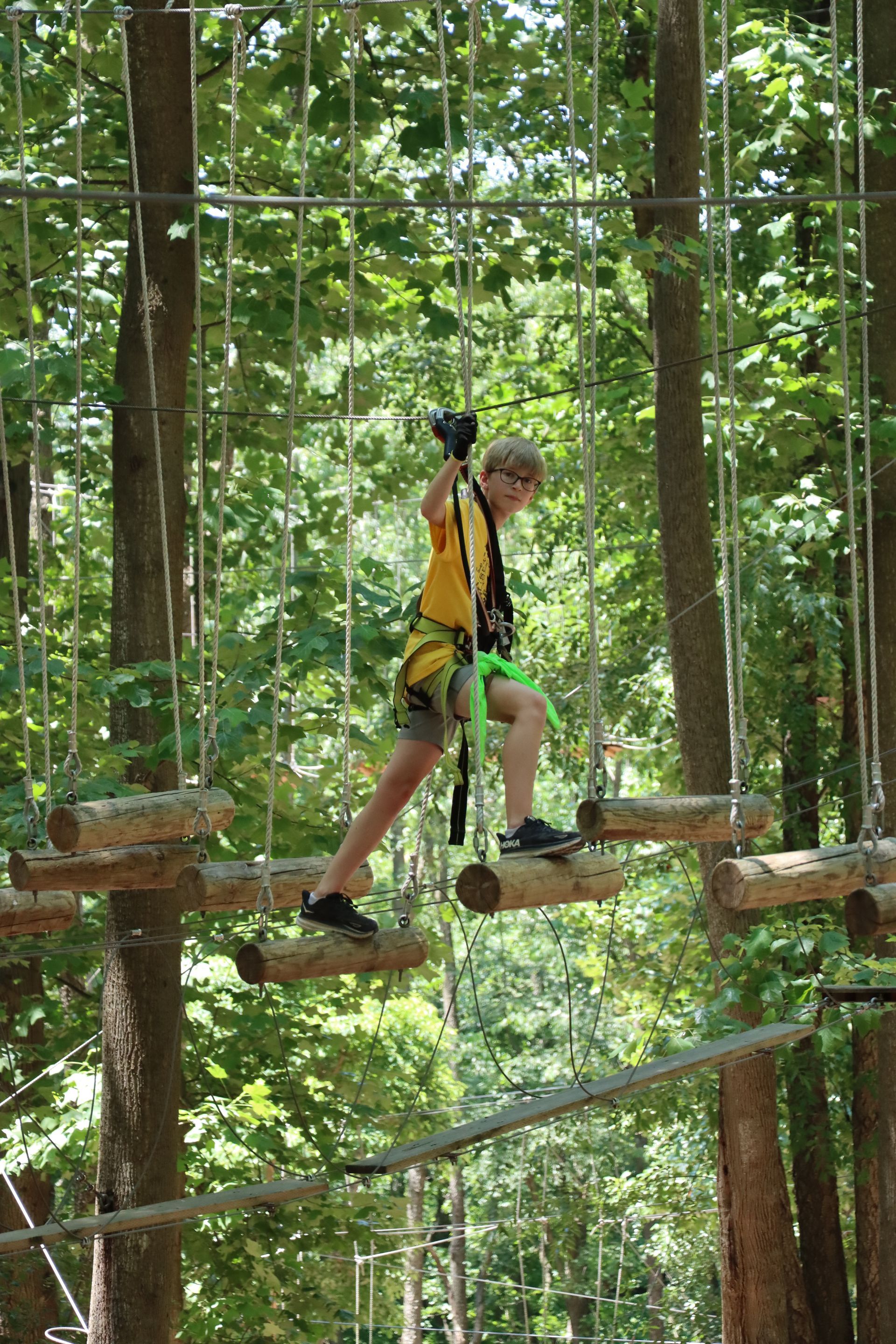 A young boy is walking across a ropes course in the woods.