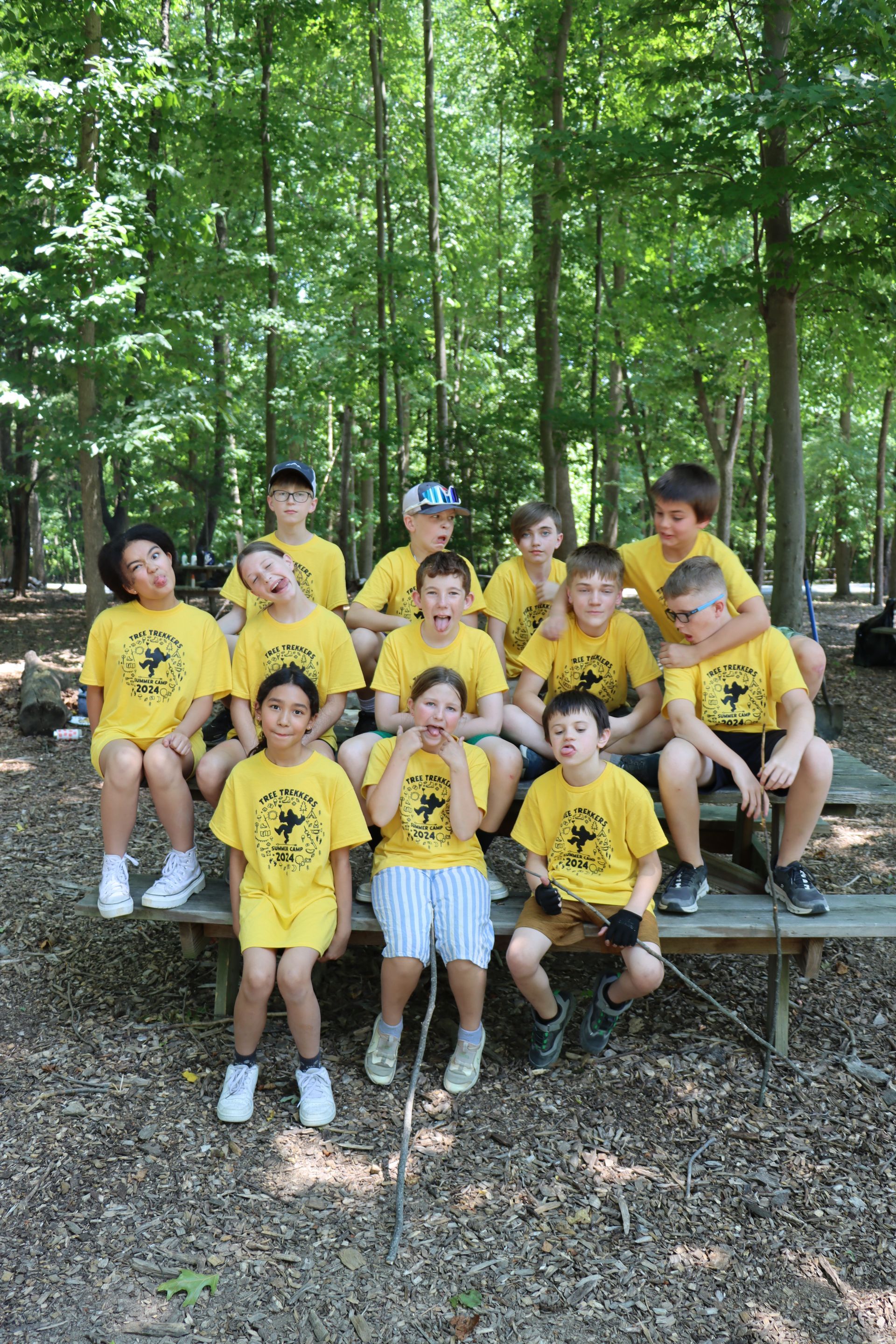 A group of children are sitting on a picnic table in the woods at summer camp