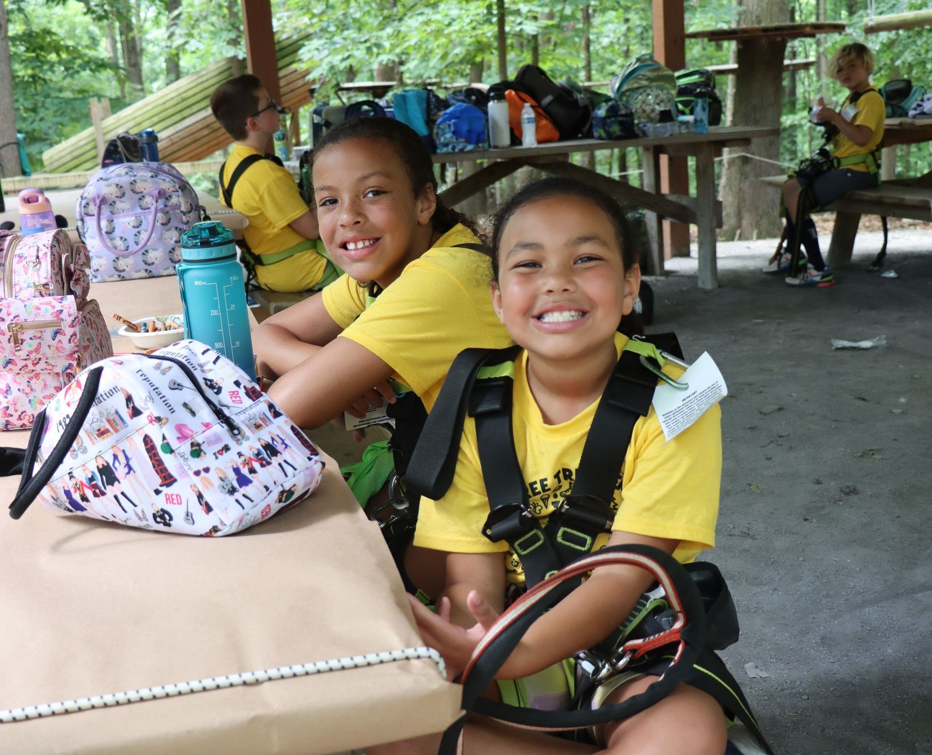 Two young girls in yellow shirts are sitting at a picnic table smiling at Tree Trekkers