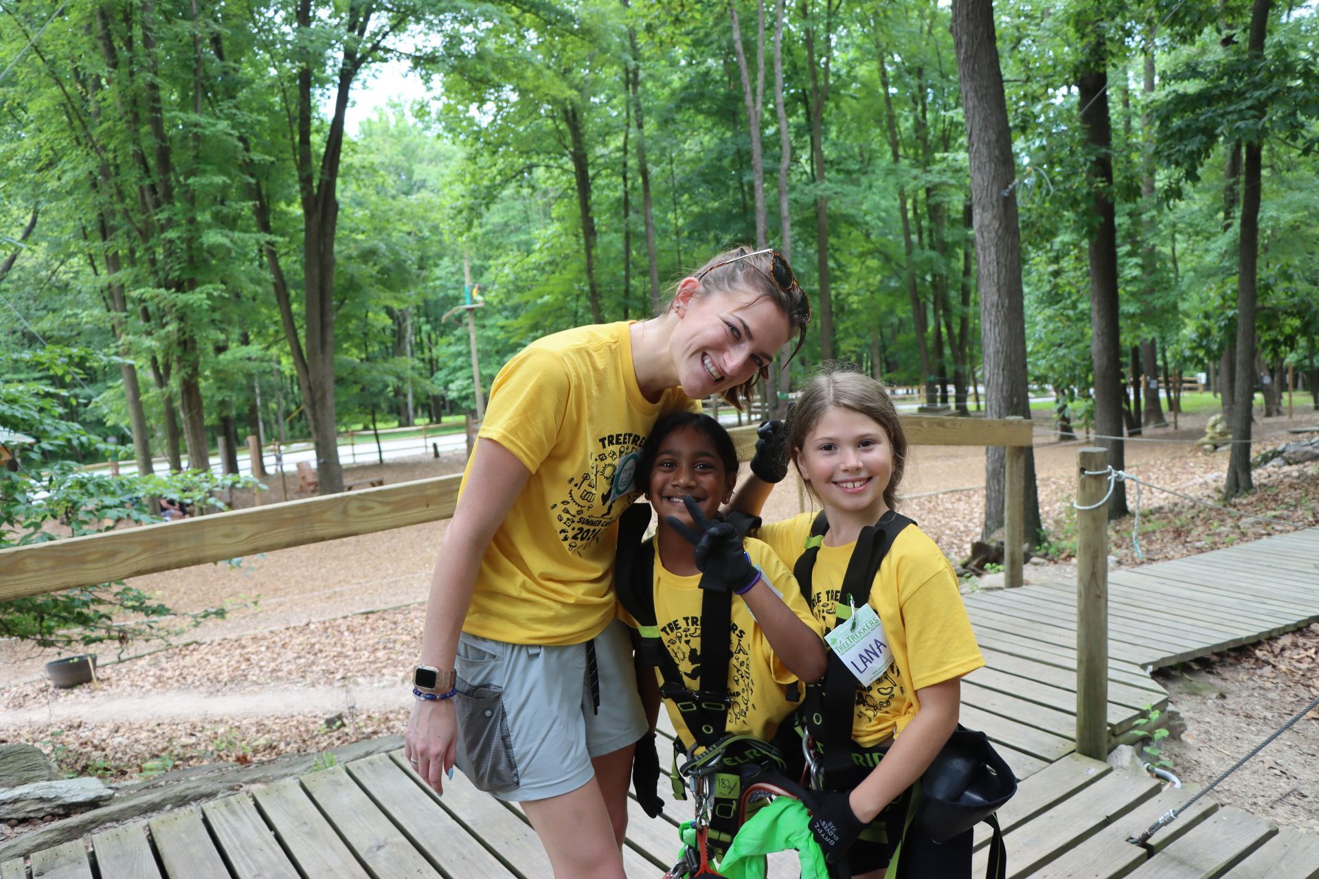 A woman in a yellow shirt is standing next to two young girls in yellow shirts at summer camp