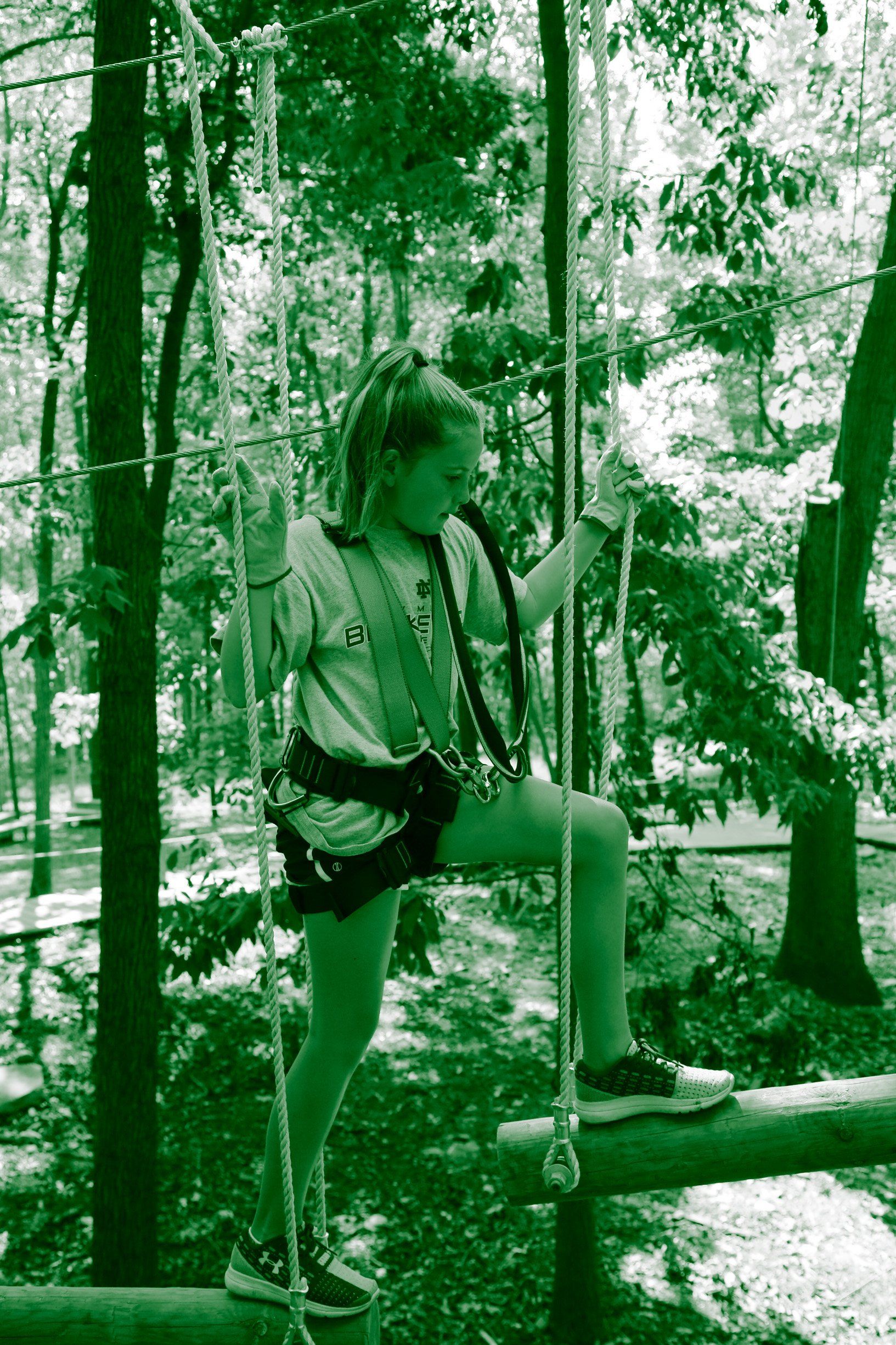 Girl climbing on green intermediate level of highropes course