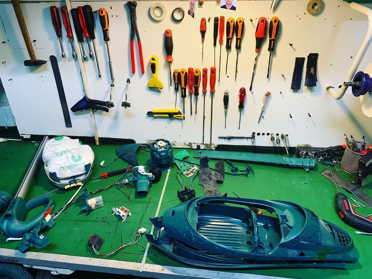 Banchi da lavoro con utensili manuali appesi e pezzi sparsi su una superficie di lavoro verde in un garage o in un'officina.