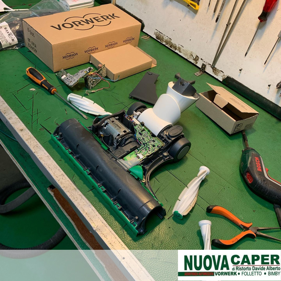 Banco da lavoro con un'auto radiocomandata smontata, attrezzi, scatole e pezzi su un tappetino verde.