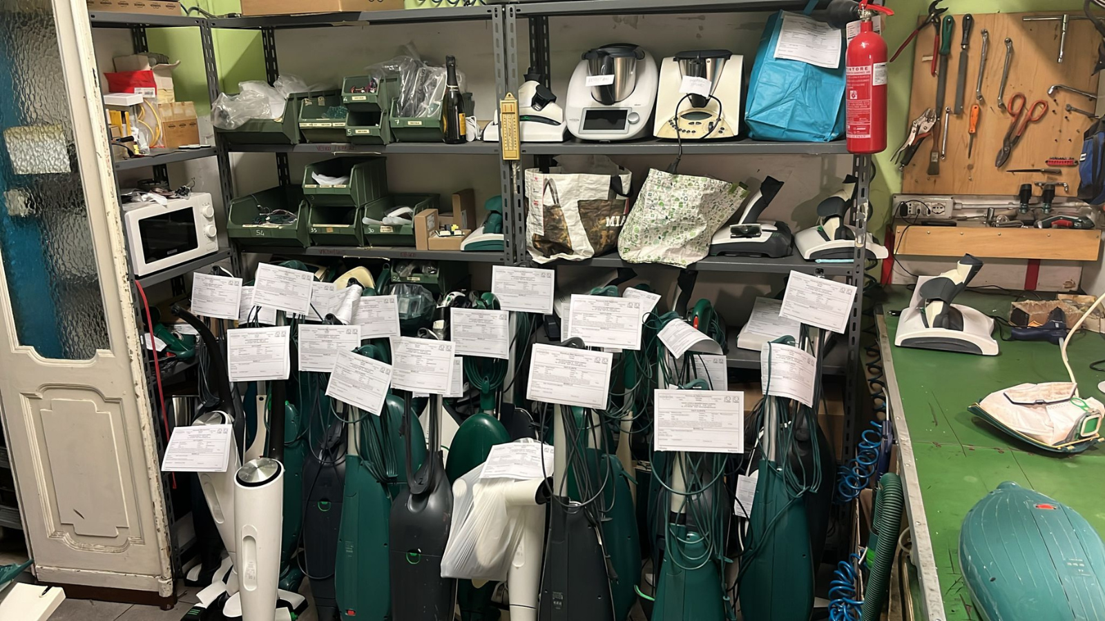 Scaffali dell'officina pieni di sacche da golf verdi con etichette bianche e attrezzi sullo sfondo.