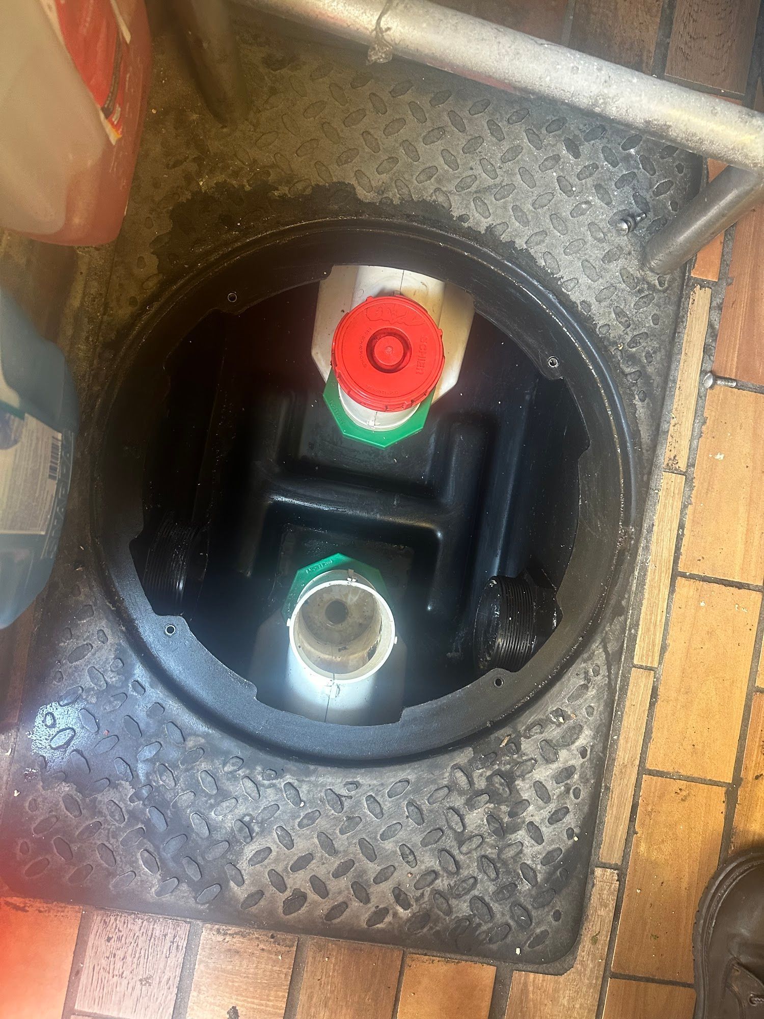 Open sewer access point with two pipes and a black interior. Red and green caps visible.