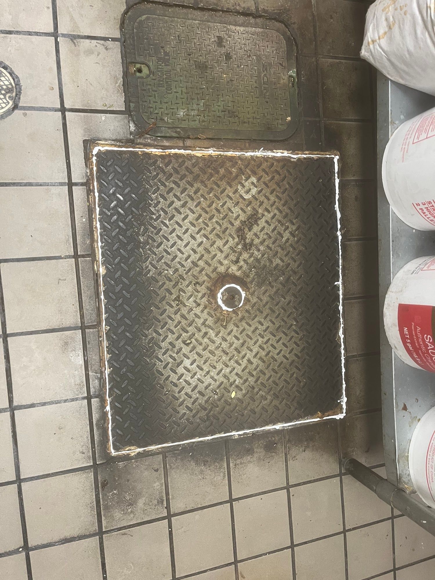 Square metal access cover on tiled floor with a smaller cover nearby.