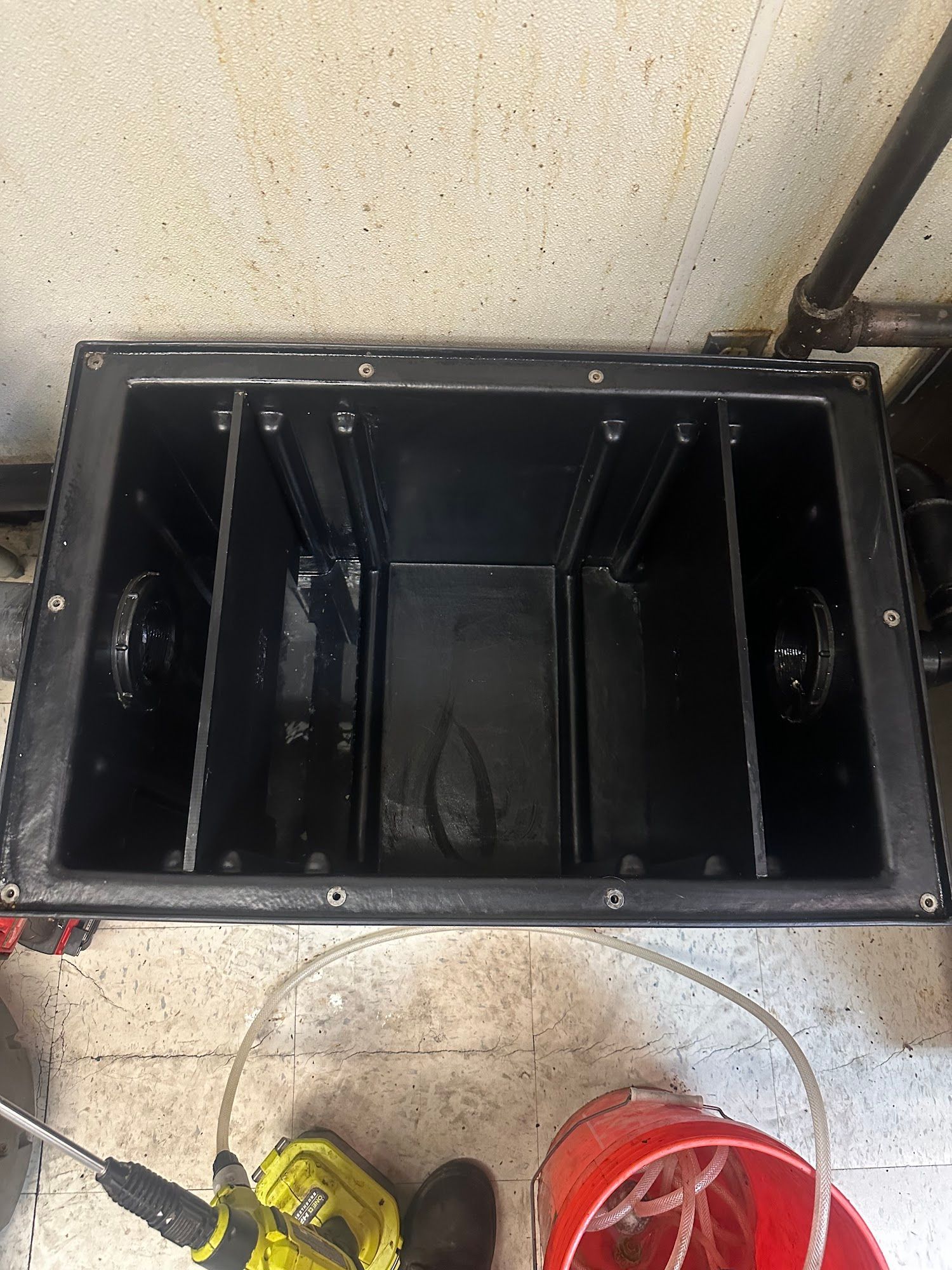 Black rectangular filter box, open, with internal compartments. Tools, bucket, and tubing nearby.