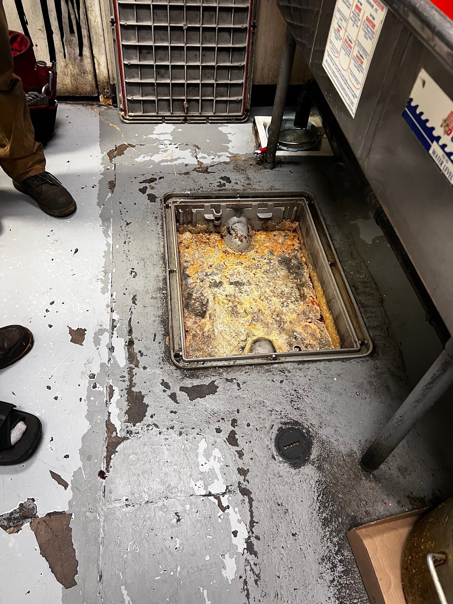 Dirty kitchen floor with food debris and an open drain cover.