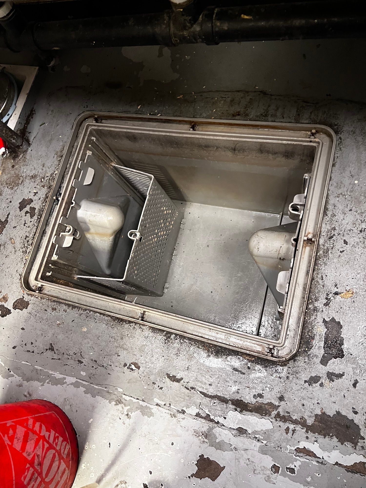 Metal access panel open on a concrete floor, revealing a light fixture within.