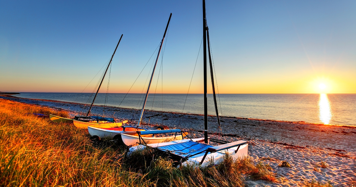 Sun setting on the coast of Cape Cod, MA, with sailboats sitting on the shoreline