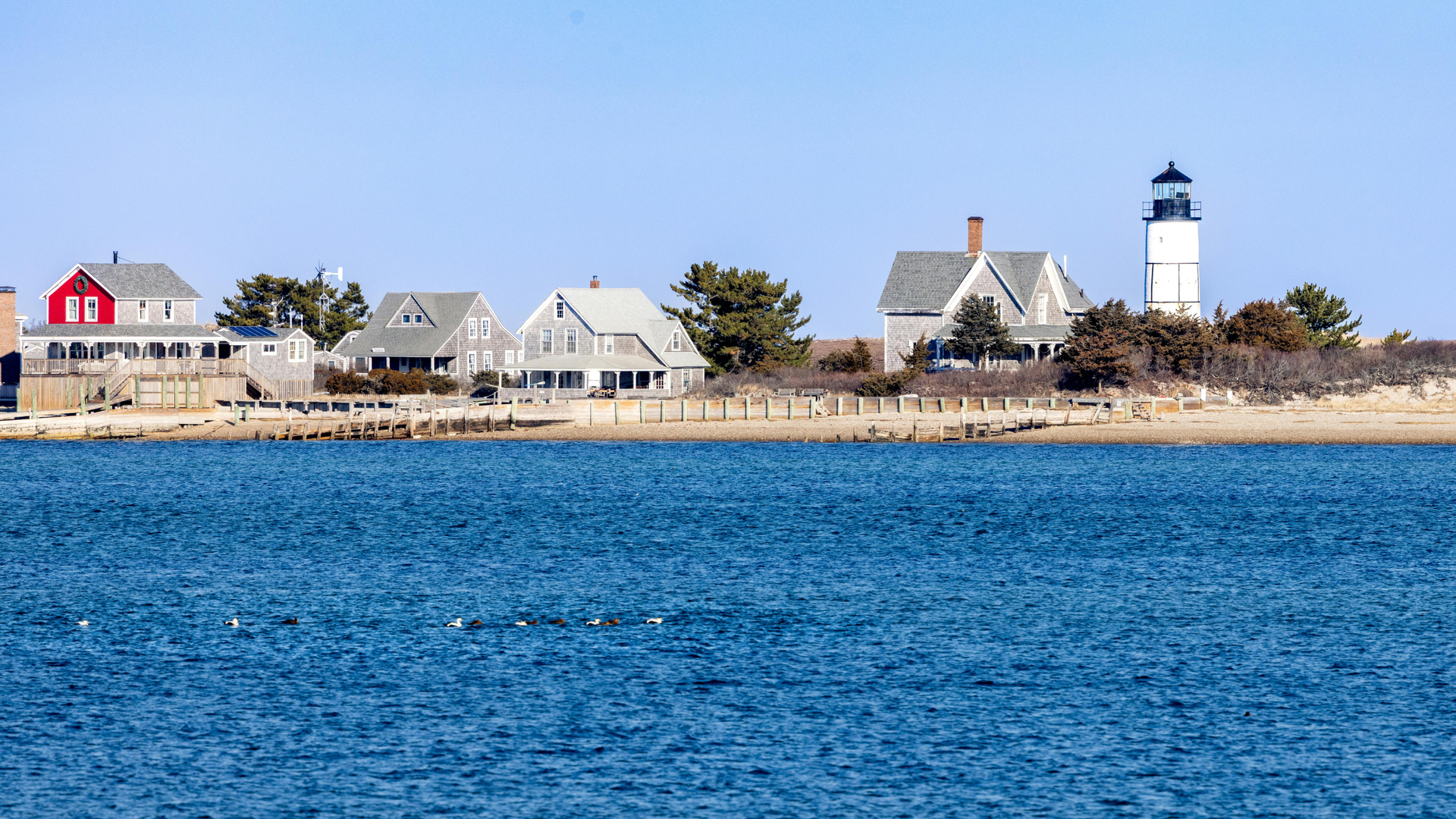 Cape Cod village with white houses and a lighthouse behind a blue ocean