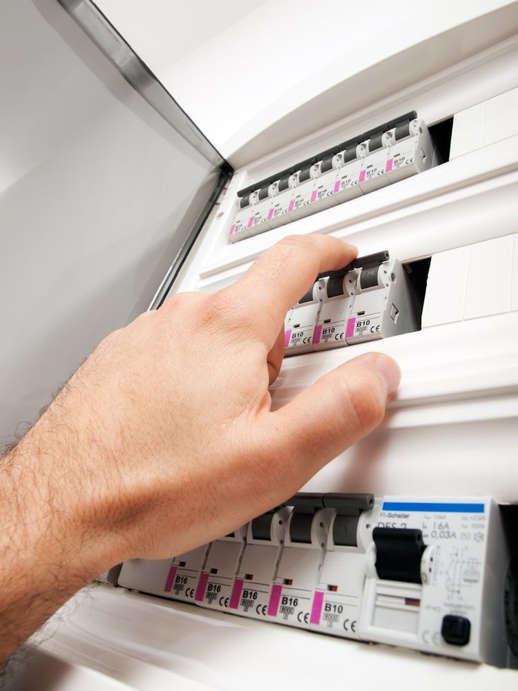 Hand flipping a circuit breaker in a white electrical panel
