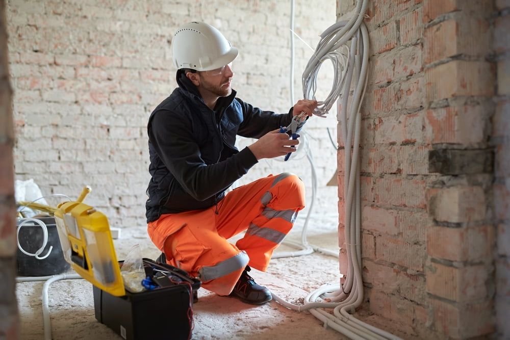 Electrician in orange workwear and hard hat working on wiring inside a building