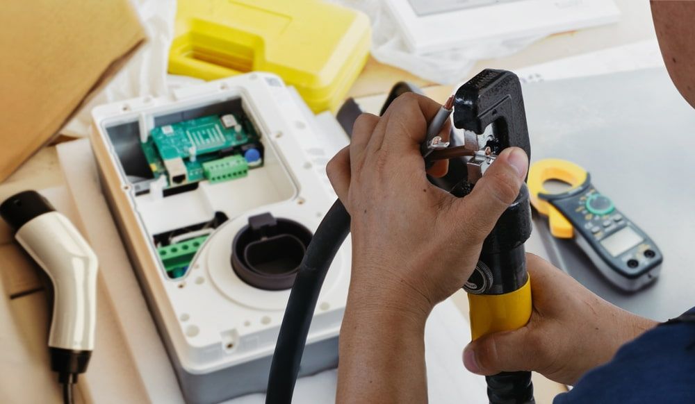 Person working on an electric vehicle charger, with a multimeter and tools