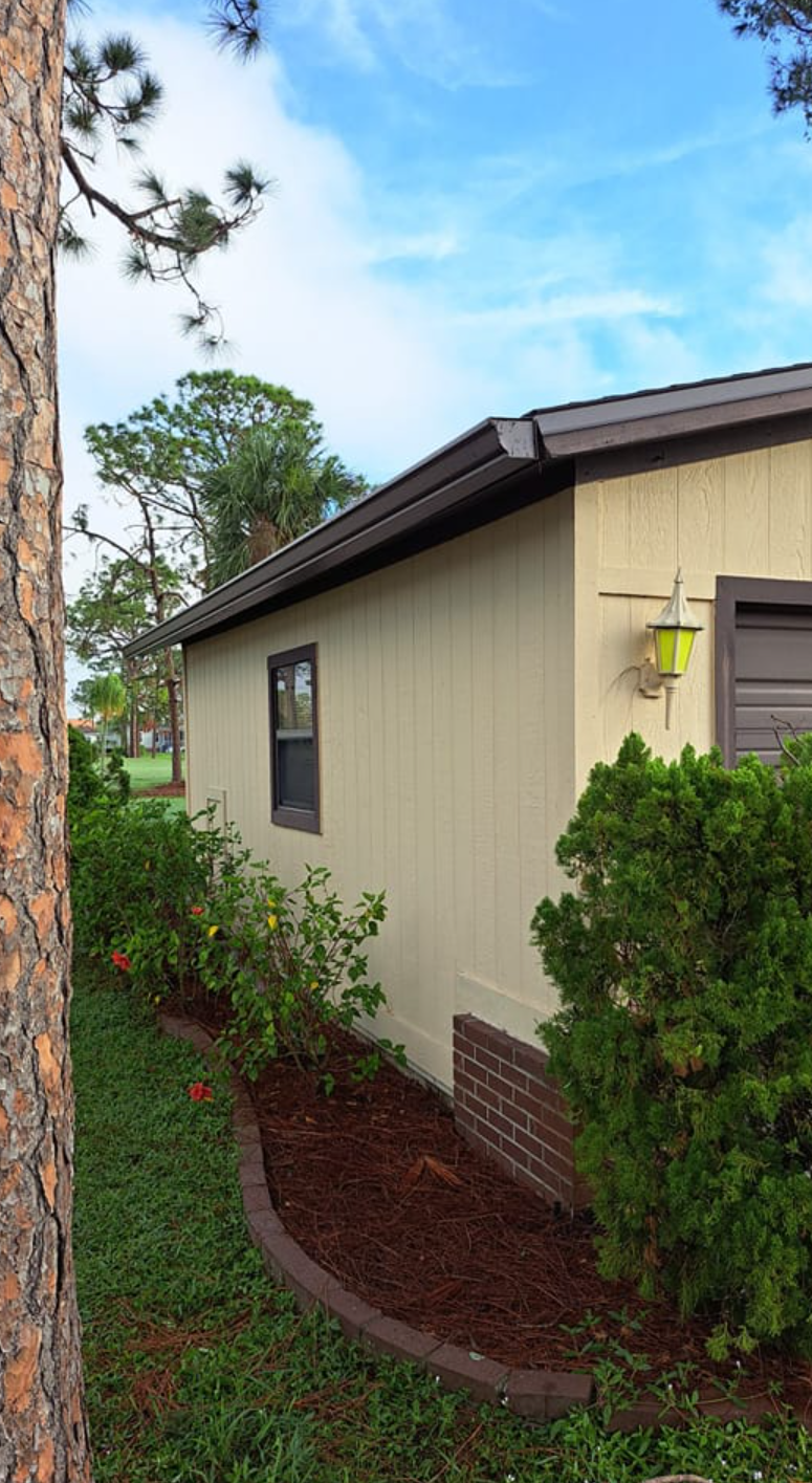 The side of a mobile home with a tree in front of it.