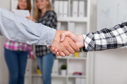 A handshake with two women in the background.