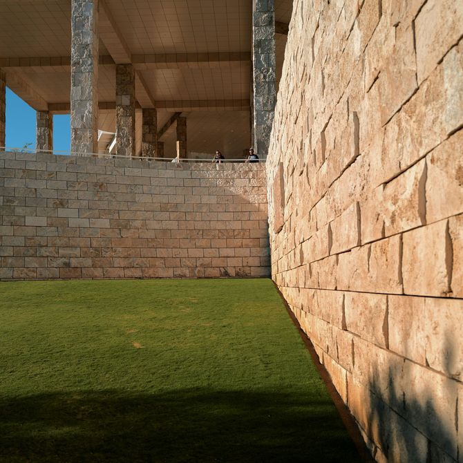 A green lawn meets two stone walls at a sharp corner, with a shaded concrete structure visible in the background.
