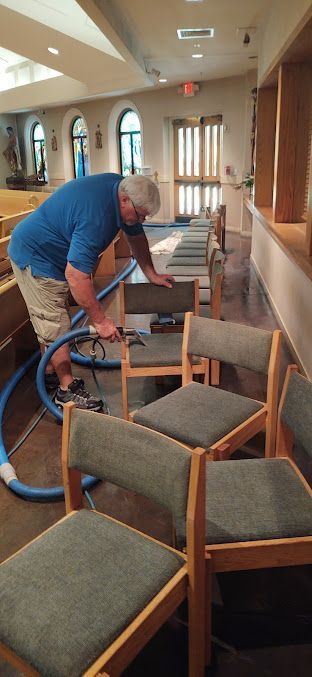 A man is cleaning chairs in a church with a vacuum cleaner.