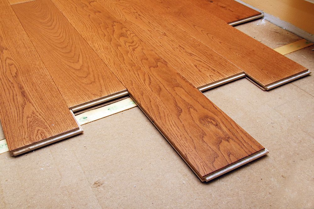 Wooden floorboards being installed on a subfloor, showing the interlocking process, with varying shades of brown. — TNT Floor Removal & Demolition in Tewantin, QLD