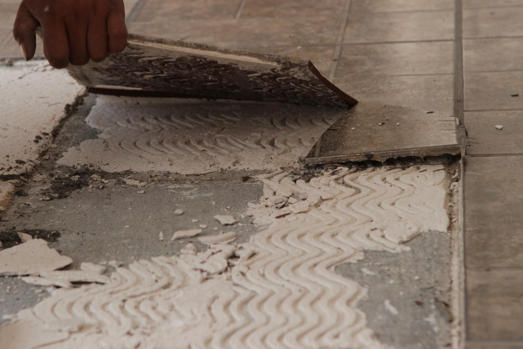 A Person Is Removing Tile on The Floor — TNT Floor Removal & Demolition in Tewantin, QLD