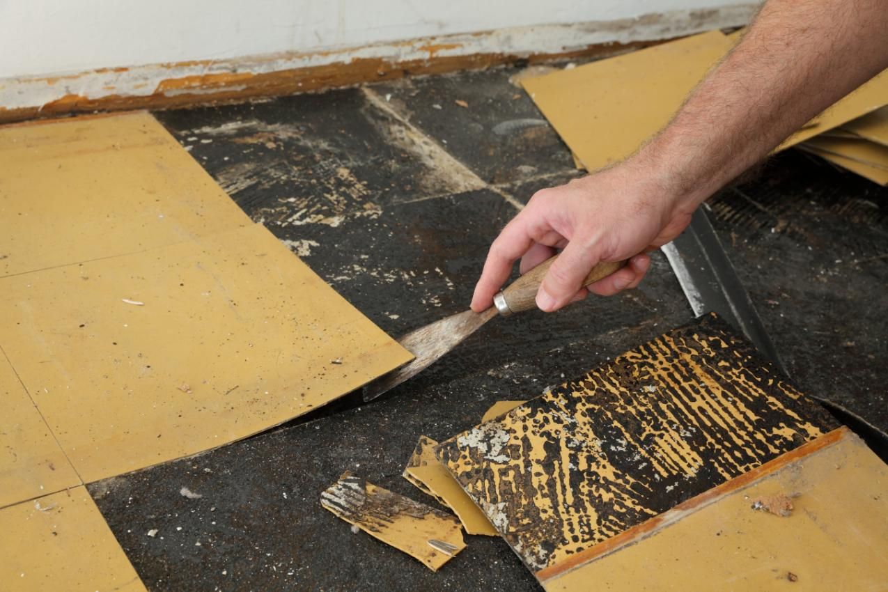 A Person Is Using a Spatula to Remove Carpet from The Floor — TNT Floor Removal & Demolition in Tewantin, QLD