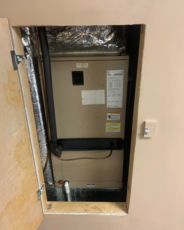 Open wall access panel showing a beige HVAC unit with foil insulation in a narrow closet.