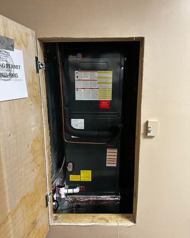 Open wall niche with a black HVAC furnace and exposed pipes in a utility closet.
