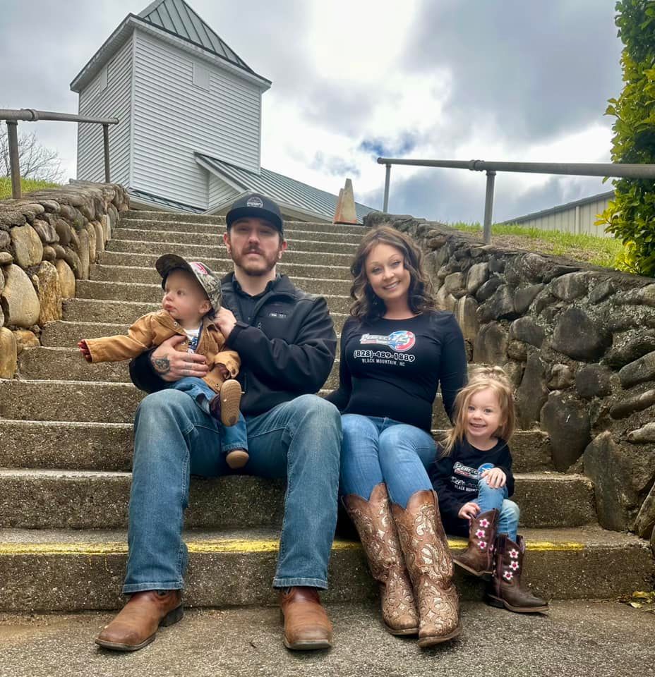 Family of four sitting on stone steps outdoors, with a small white tower in the background.